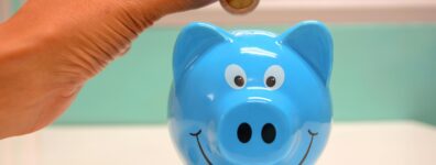 Hand inserting a coin into a blue piggy bank for savings and money management.