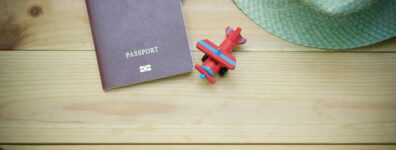 Flat lay of a passport, straw hat, and toy airplane on a wooden surface.