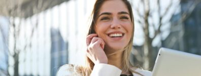 Confident businesswoman using her tablet and phone, smiling outdoors in sunlight.